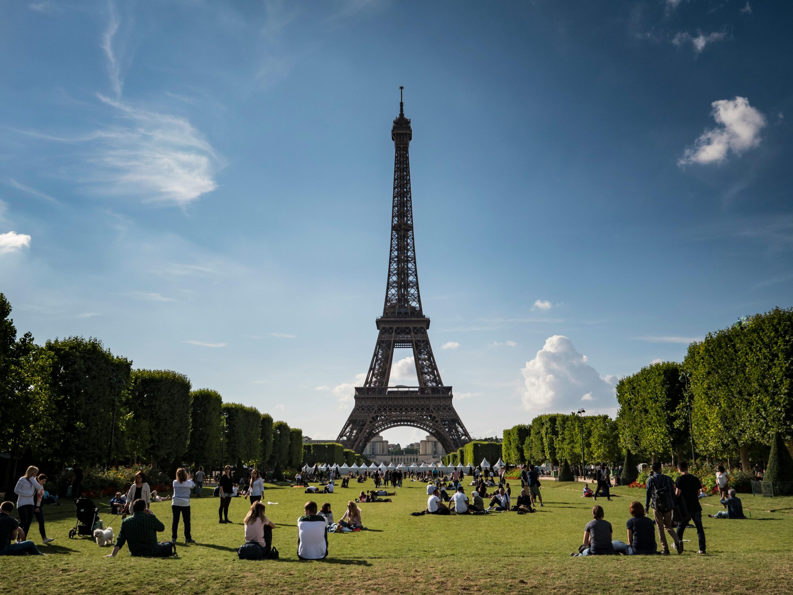 View of Eiffel Tower on a sunny day with people relaxing in a Paris park.